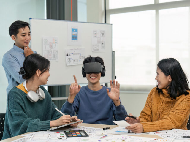 Diverse development team testing virtual reality headset, brainstorming on augmented reality improvement, future technology
